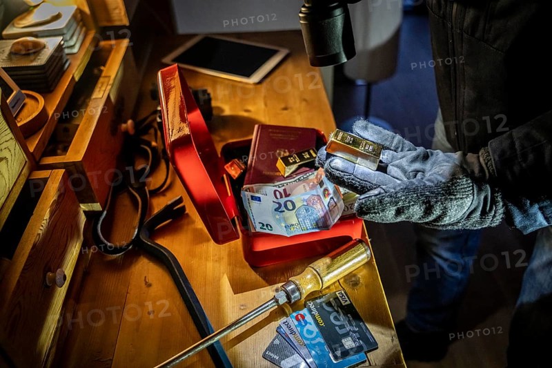 Symbolic image of a burglary, perpetrator has broken into a flat from the garden side and is looking for loot, breaks open a cash box, finds valuables, money