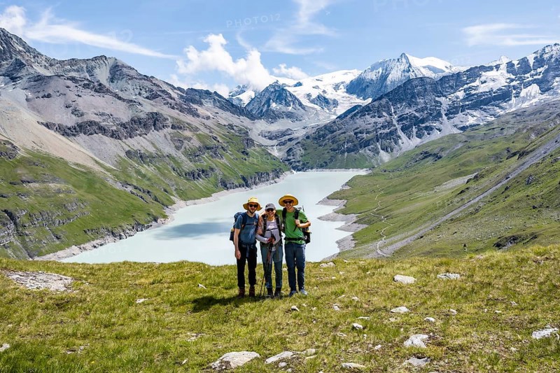 Three friends, mountaineers in front of a blue mountain lake, reservoir Lac des Dix, behind mountain peak Mont Blanc de Cheilon with glacier, Hérménence, Valais Alps, Valais, Switzerland, Europe