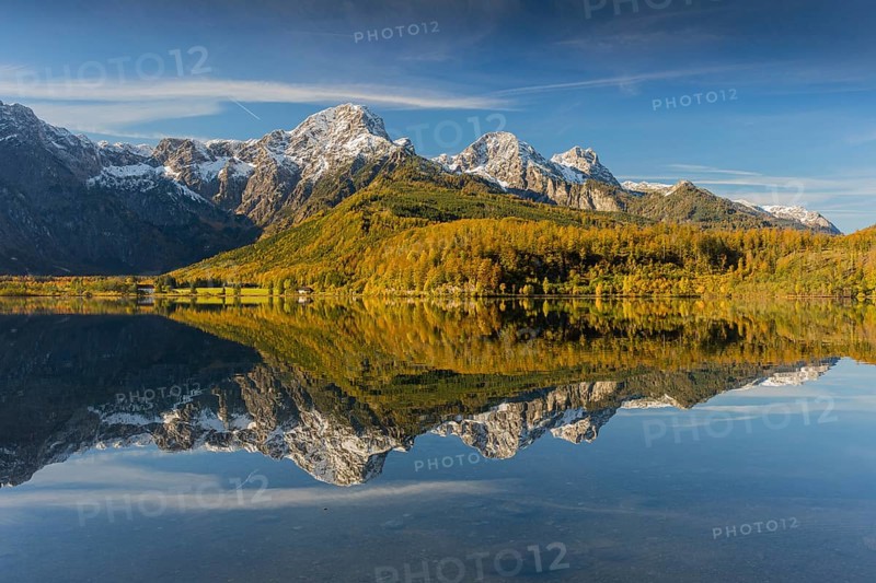 Lake Almsee in autumn with mountains reflected in the lake. Blue sky