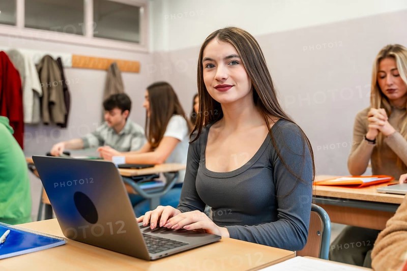 Young woman using laptop in university classroom, participating in an engaging lesson with her classmates