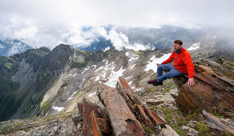 Mountaineer sitting on a rock, cloudy mountain landscape at the summit of Lasörling, view to Berger Kees and mountain peak Schober, Lasörling Group, Hohe Tauern National Park, East Tyrol, Tyrol, Austria, Europe