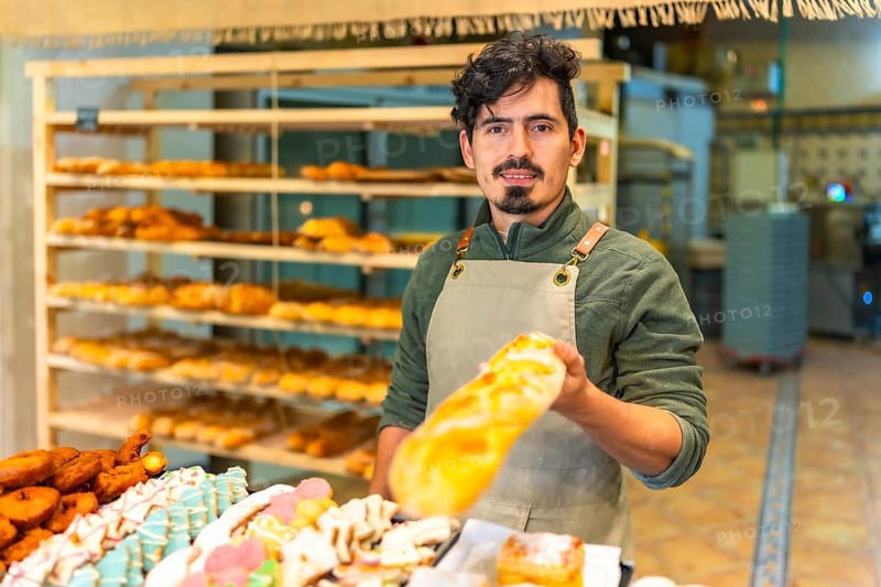 Latin young friendly baker offering freshly baked baguette in an artisan bakery shop