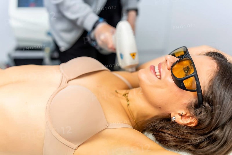 Beautiful and attractive adult woman receiving depilatory treatment on armpit lying on the clinic