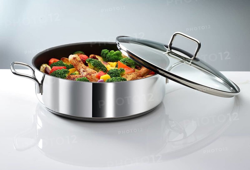 Cooking pot with vegetables and chicken thighs in front of a white background, studio shot