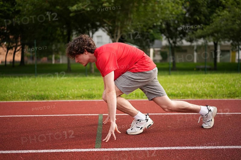 Side view full length of a caucasian young male runner in the starting line of a track ready to start running