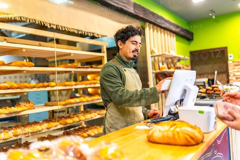 Salesman using touchscreen computer to calculate the bill of a client in the counter of bakery shop