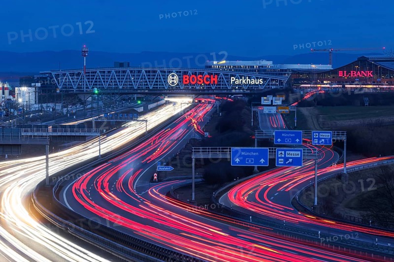 A8 motorway at Stuttgart Airport in the evening. Heavy traffic, lanes of light. Modern architecture of Messe Stuttgart with multi-storey car park above the motorway lanes. Logo of the Bosch company. Stuttgart, Baden-Württemberg, Germany, Europe