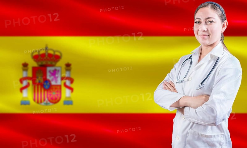 Female doctor on Spain flag. Doctor with crossed arms on Spain flag. Spain Health and Care concept