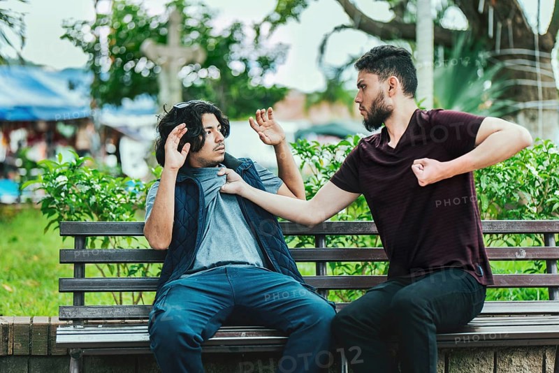 Two male friends arguing on a park bench. Two guys arguing sitting on a bench