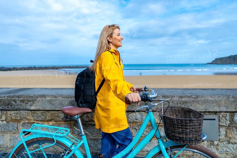 Tourist walking with her bicycle along the beach promenade on a cloudy day, enjoying the seascape