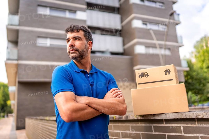 Portrait of a confident delivery man with arms crossed standing looking away next to parcels in the city