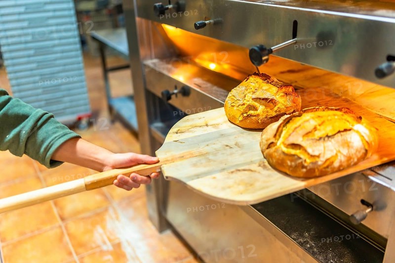 Latin unrecognizable man removing baked artisan bread from oven in a bakery kitchen