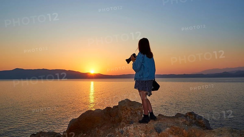Sunrise, sun reflection on the sea, orange-blue cloudless sky, girl from behind with jeans jacket and camera in hand, Rodopou peninsula, Gramvoussa peninsula, Pirate Bay, Balos, Tigani, West Crete, island of Crete, Greece, Europe