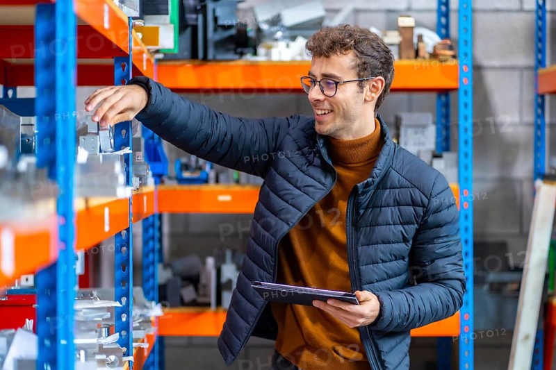 Proud engineer in the stock room of a cnc factory using tablet and smiling