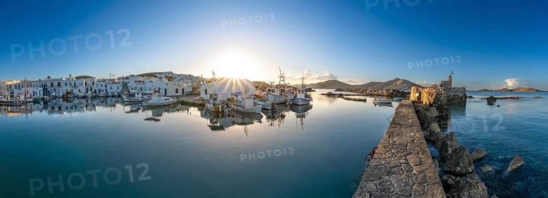 Panorama, fishing boats in the harbour of Naoussa at sunset, reflected in the sea, sun star, ruins of the Venetian castle on the right, white Cycladic houses, Naoussa, Paros, Cyclades, Greece, Europe