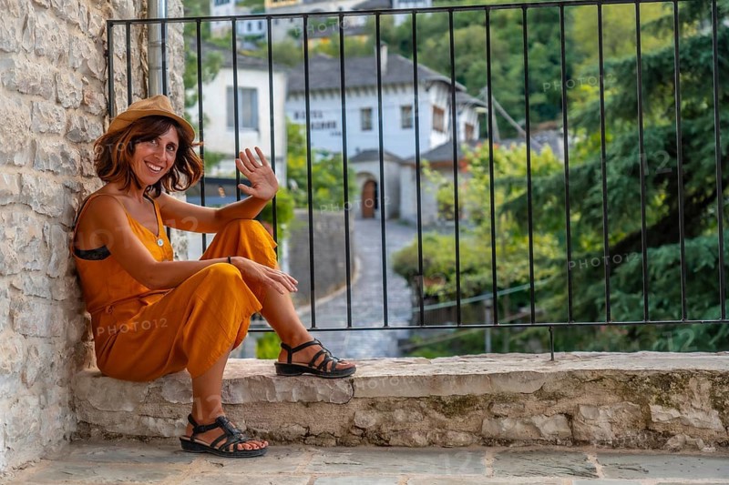 Portrait of a tourist woman sitting waving at a viewpoint the city of Gjirokaster or Gjirokastra. Albanian