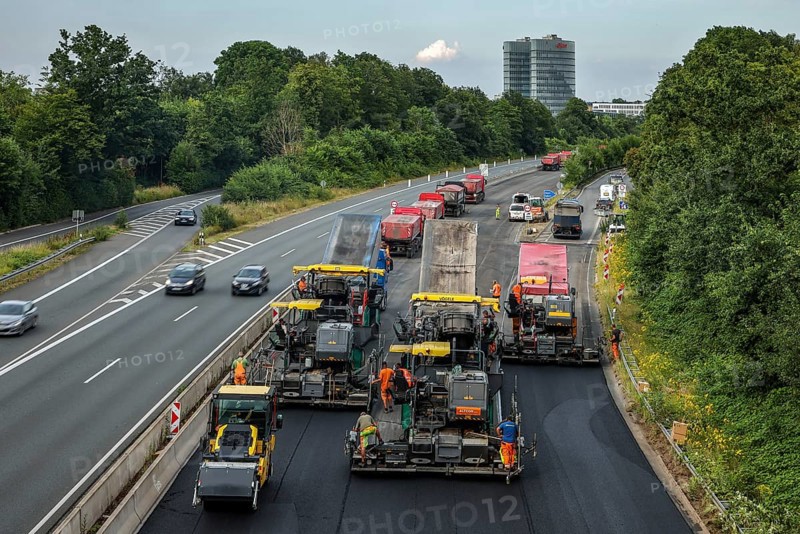 Essen, North Rhine-Westphalia, Germany, road construction, asphalt pavers and road rollers laying new, open-pored, whisper asphalt on the A52 motorway, here between the Essen-Kettwig and Essen-Rüttenscheid junctions in the direction of Dortmund. Skyline of Essen with the EON headquarters building in the background, Europe