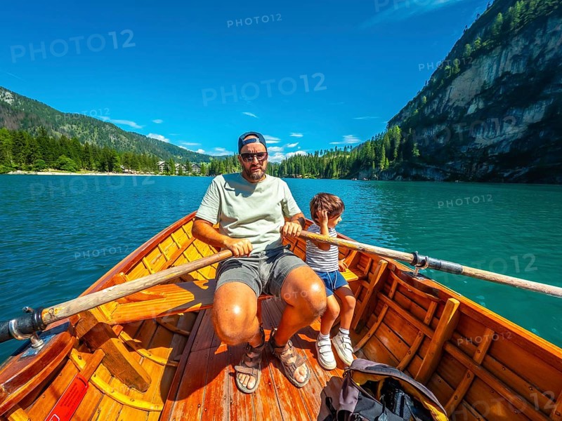 Tourists rowing a wooden boat on lake braies, surrounded by stunning mountain scenery in the italian dolomites