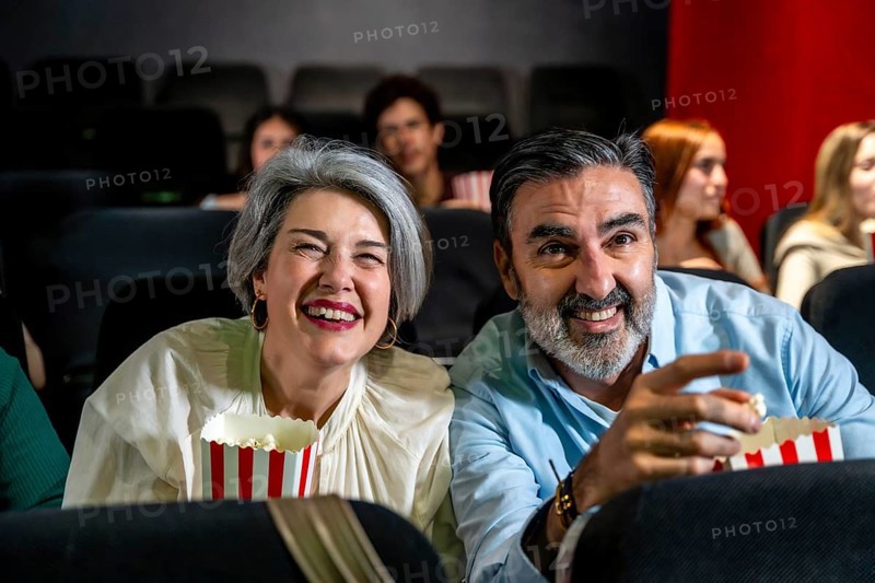 Happy mature couple laughing and having fun watching a movie at the cinema, eating popcorn