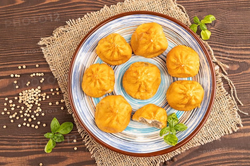 Fried manti dumplings with pepper, basil on brown wooden background and linen textile. Top view, flat lay, close up