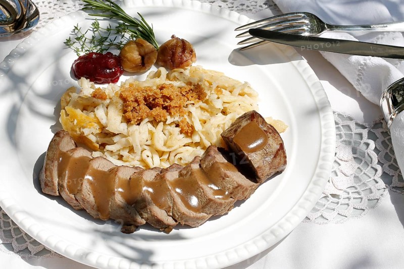 Swabian cuisine, roast venison with spaetzle, chestnuts and breadcrumbs, breadcrumbs, saddle of venison arranged on a plate, gravy, game dish, meat, main course, gravy, cutlery, knife, fork, grandmother's kitchen, regional, home cooking, typical Swabian, traditional cuisine, festive tablecloth, food photography, studio, Germany, Europe
