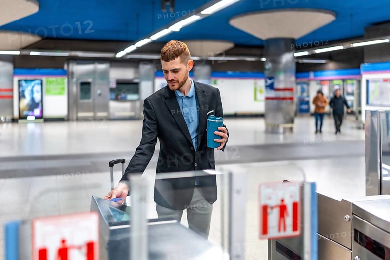 Businessman holding reusable coffee cup and using contactless credit card to enter subway station