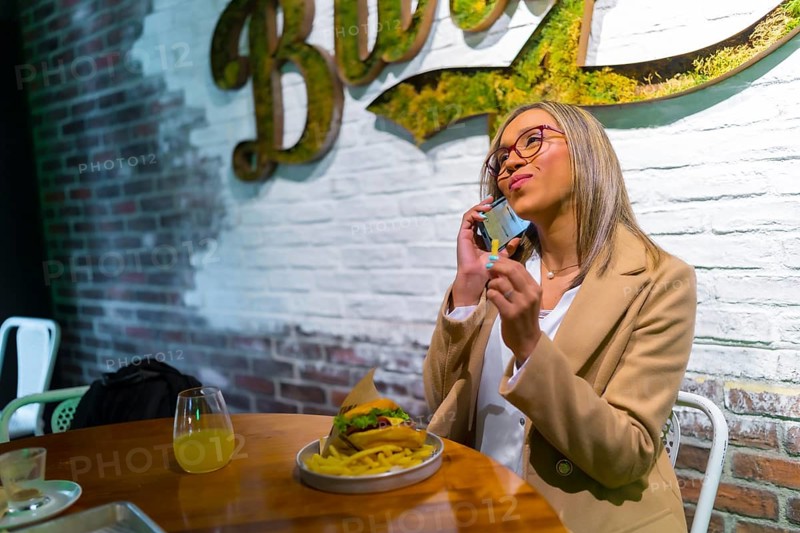 Happy latin businesswoman taking a break from work eating hamburger in a restaurant