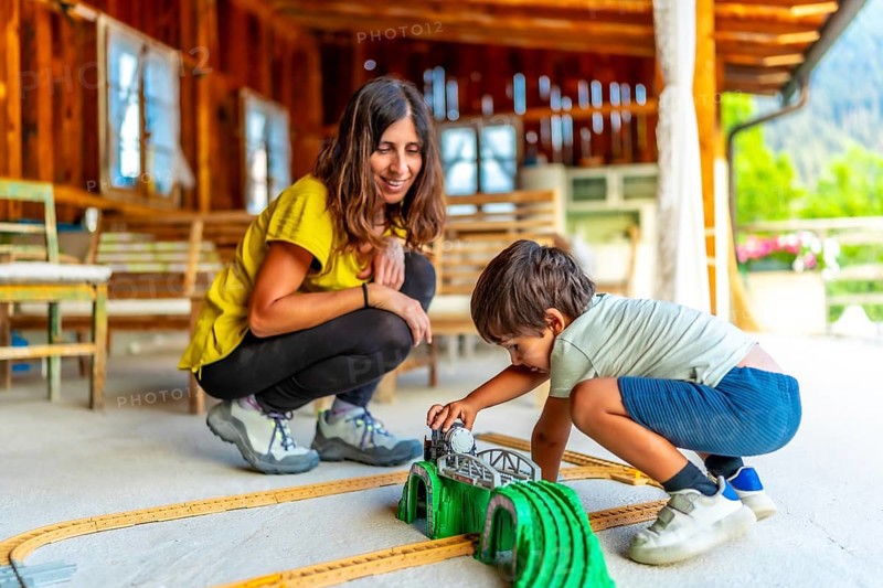 Mother and son enjoying quality time, playing with a toy train set on a rustic porch