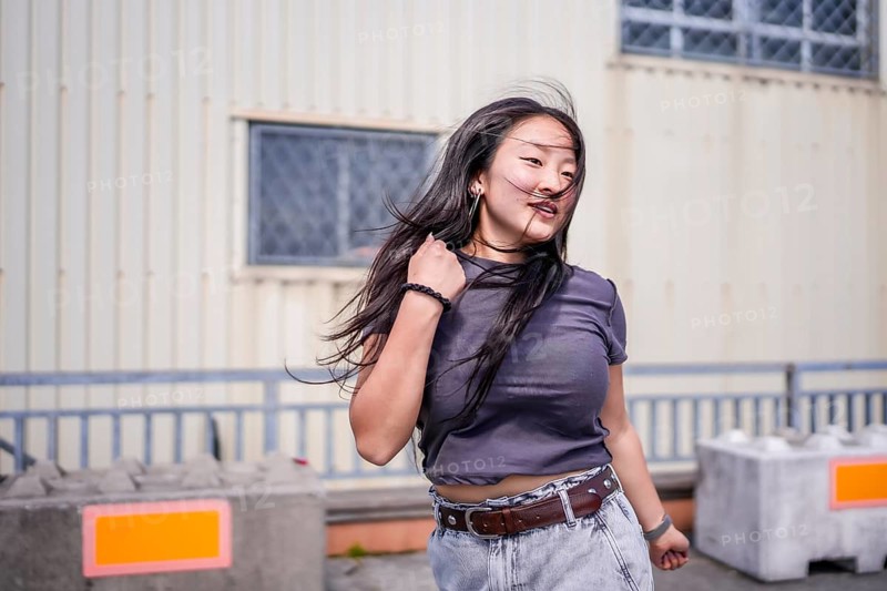 Three quarter length photo of a young cool asian girl dancing k-pop outdoors in an industrial building