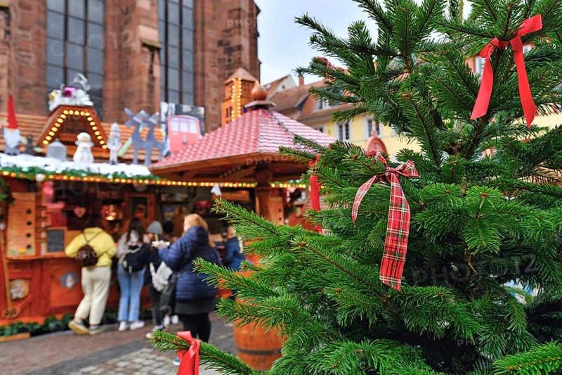 Heidelberg, Germany, December 2019: Close up of red ribbon tied to Christmas tree with sales booth and people in blurry background on traditional German Christmas market, Europe