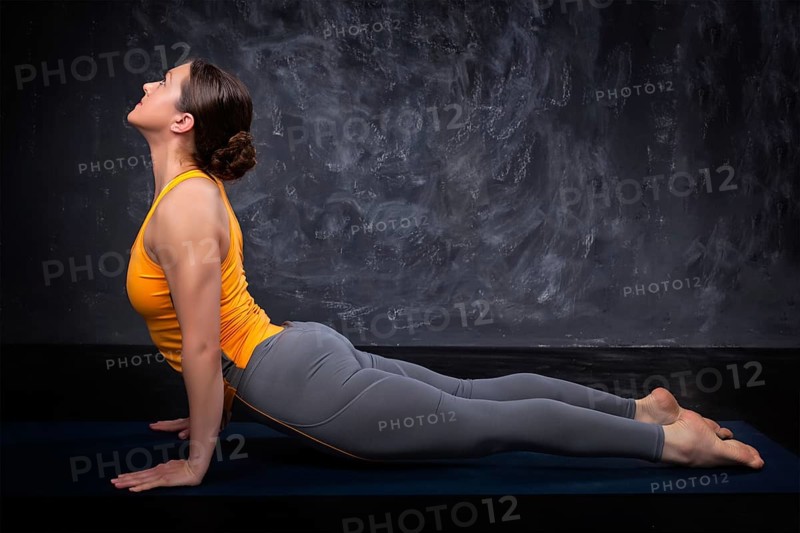 Beautiful sporty fit yogini woman practices yoga asana urdhva mukha svanasana, upward facing dog pose on dark background
