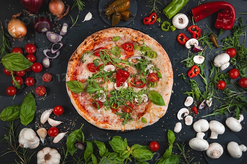 Colourful pizza topped with basil, tomatoes, rocket and mushrooms surrounded by ingredients