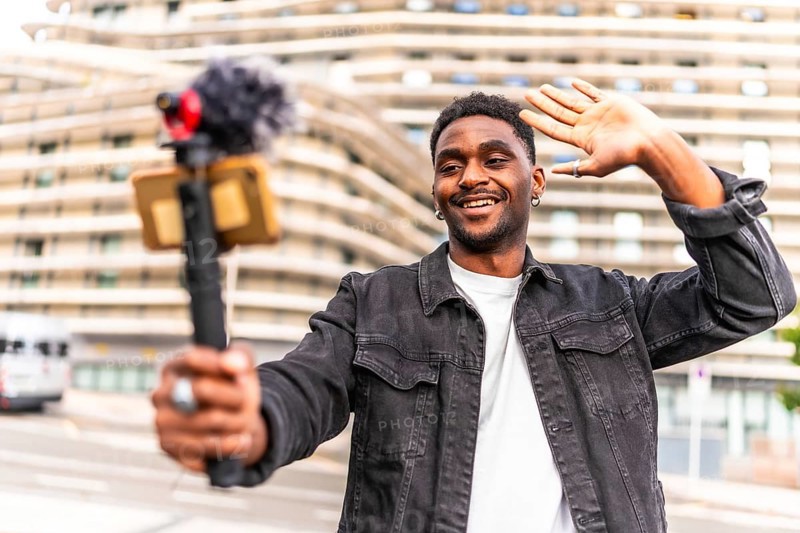 Young African man waving while filming a video blog in the city
