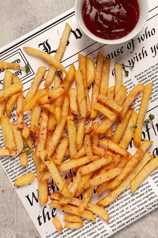 Fried French fries, scattered on a newspaper, with red sauce, top view, no people