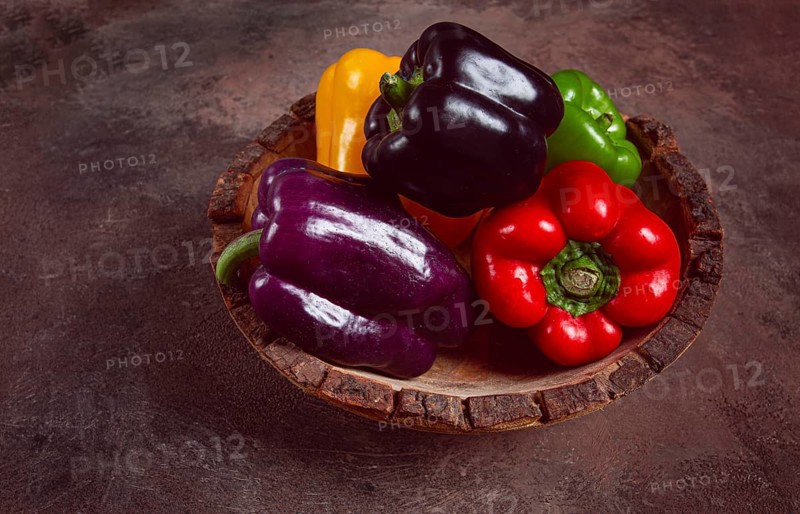 A collection of colorful bell peppers, in a wooden bowl, on a dark surface, top view, no people