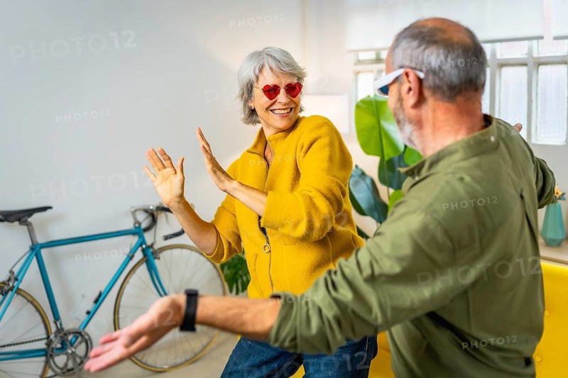 Modern senior couple with stylish sunglasses having fun together at home laughing and dancing