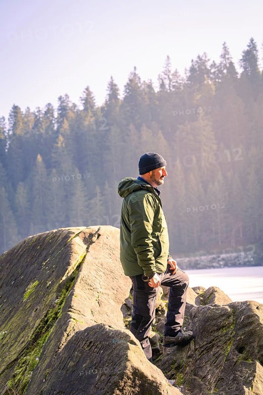 Man with outdoor clothes standing on a rock, surrounded by forest and sunlight, Glaswaldsee, Bad Rippoldsau-Schapbach, district of Wolfach, Black Forest, Germany, Europe