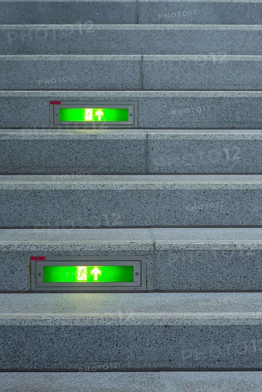 Public staircase with green illuminated emergency exit signs, Germany, Europe