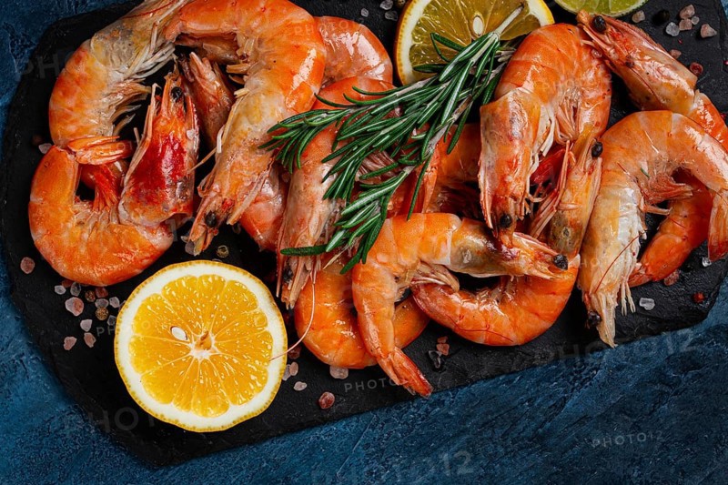 Freshly frozen shrimp, with lemon and rosemary, on black slate, close-up, top view, no people