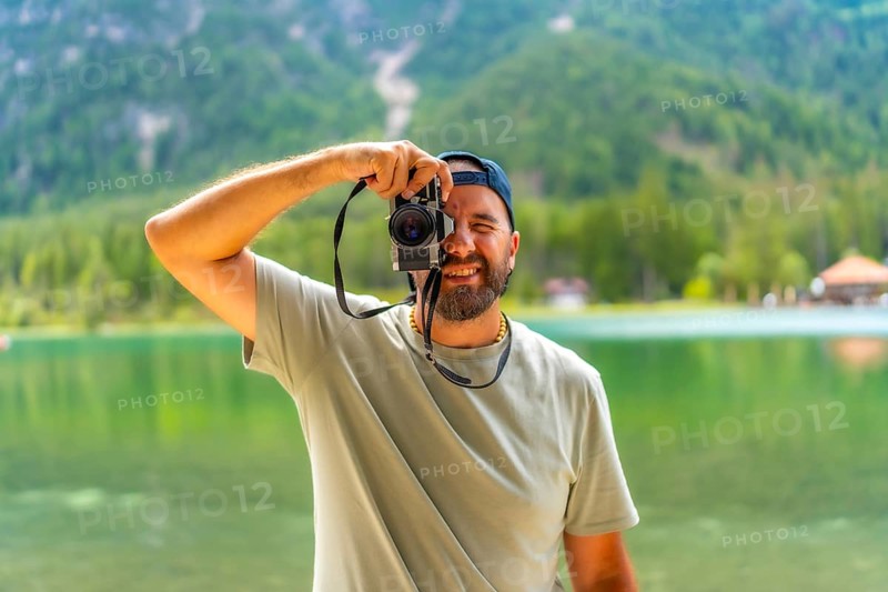 Tourist taking pictures with vintage camera at lake dobbiaco, surrounded by the breathtaking scenery of the dolomites in summer
