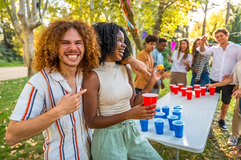 Man pointing at a female african friend that wins playing beer pong at park
