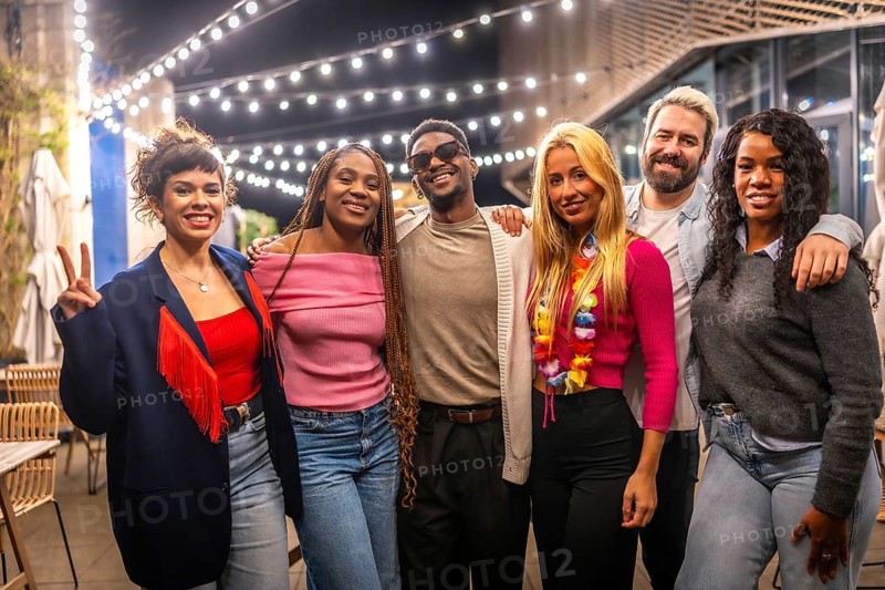 Portrait of multi-ethnic young friends standing smiling at camera in a bar terrace at night