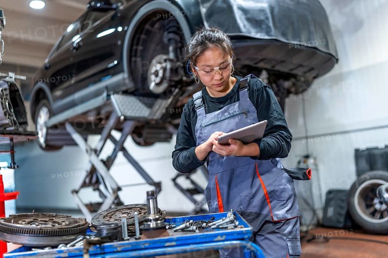 Young woman mechanic using a digital tablet, inspecting car parts and components in a professional workshop, ensuring efficient vehicle maintenance