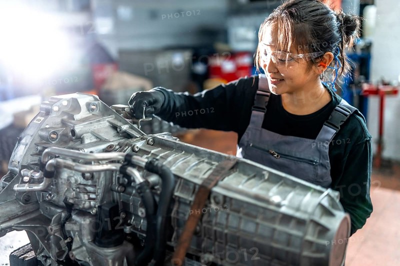 Asian woman mechanic working diligently on a vehicle gearbox in a professional garage, showcasing skill and expertise in automotive repair