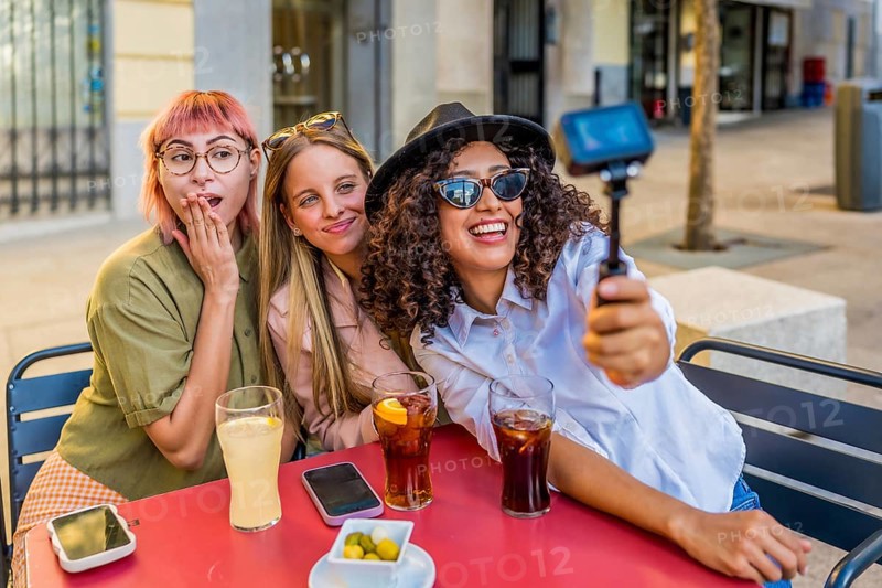 Latin beauty Woman recording video with camera while sitting with friends on a terrace drinking beverages