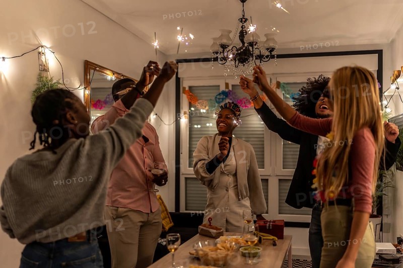 Multi-ethnic happy friends raising burning sparkler celebrating party at night at home