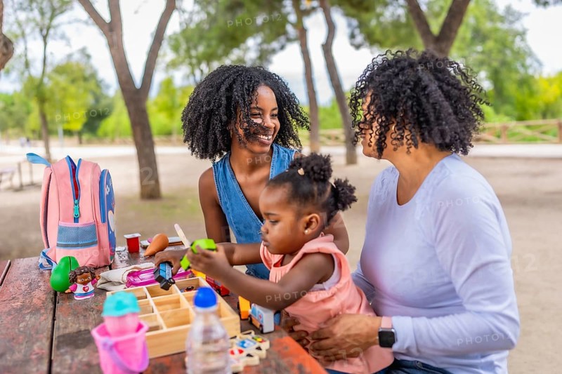 Happy african girl playing with toys sitting in a park with her mother and grandmother