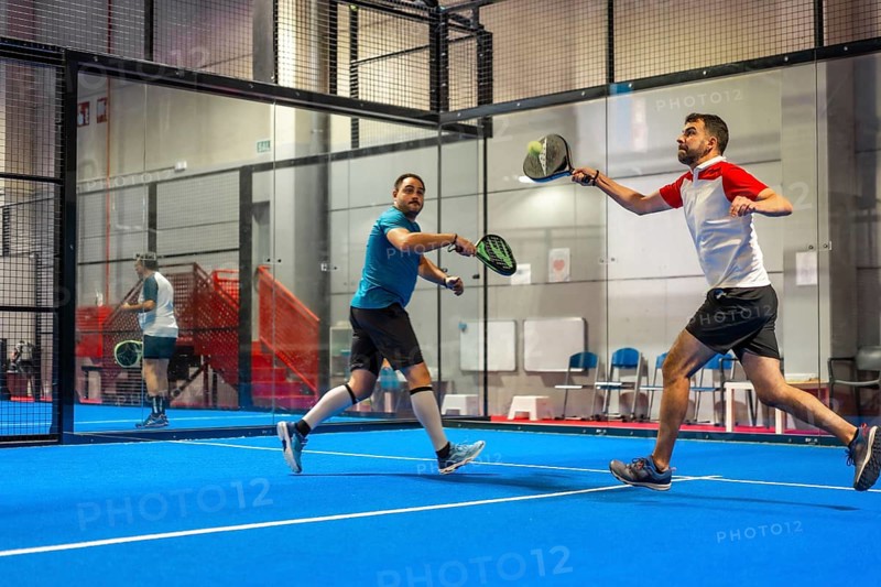 Mature caucasian male friends playing paddle tennis energetically in a blue indoor court