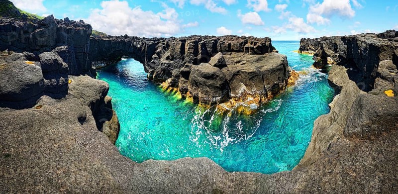 Panoramic view of rugged lava rock formations with a natural arch over turquoise sea under blue sky, A Porta do Diabo, Sao Miguel Island, Azores, Portugal, Europe