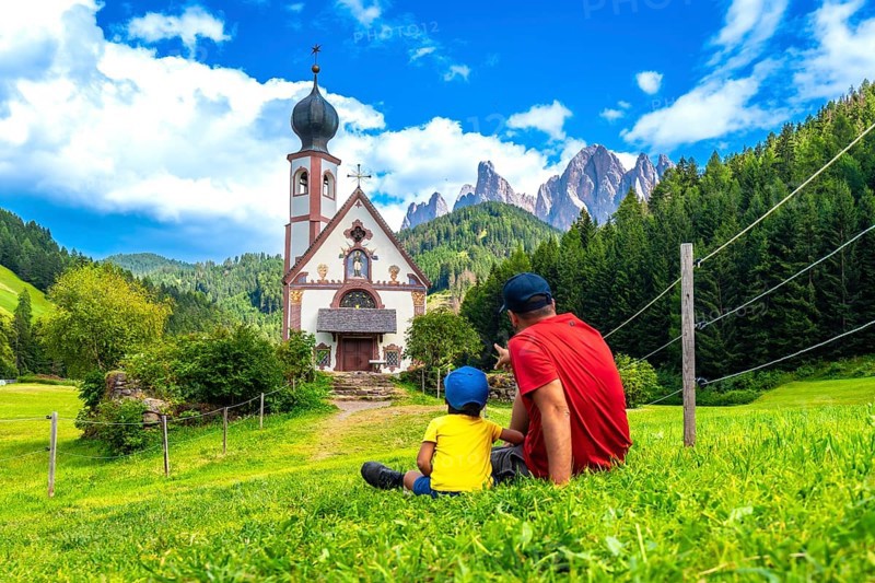 Father and son admiring the stunning view of the idyllic st. Magdalena church in the picturesque val di funes, framed by the dolomites